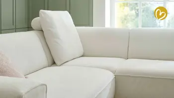 Detailaufnahme einer hellen Sofaecke mit abnehmbarem Rückenkissen und Kopfstütze, umgeben von grün getäfelter Wand und großem Fenster mit natürlichem Lichtern